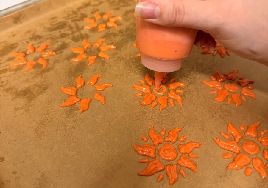 Orange batter being piped into sunburst designs on a parchment-lined baking pan.